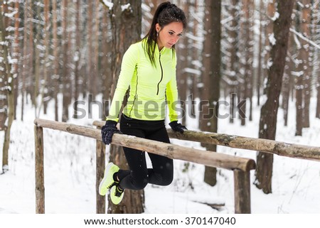 Fit woman exercising outdoors doing triceps dips on parallel bars at park. Street workout winter