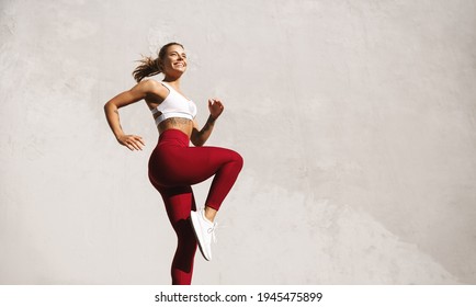 Fit woman exercising outdoors. Healthy young female athlete doing fitness workout. Sportswoman raising leg, do functional training outside on bright sunny day, smiling pleased, wearing sport outfit - Shutterstock ID 1945475899