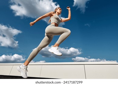 Fit woman exercising outdoors. Healthy young sportswoman doing fitness. An athlete makes jumps, does functional training on the street on a bright sunny day, smiles contentedly, in a sports suit - Powered by Shutterstock