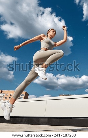 Fit woman exercising outdoors. Healthy young sportswoman doing fitness. An athlete makes jumps, does functional training on the street on a bright sunny day, smiles contentedly, in a sports suit