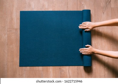 Fit Woman Folding Blue Exercise Mat On Wooden Floor Before Or After Working Out In Yoga Studio Or At Home. Equipment For Fitness, Pilates Or Yoga, Well Being Concept. Flat Lay, Space For Text.