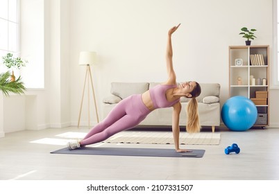 Fit Woman Having Fitness Workout At Home. Slim Young Caucasian Lady In Modern Light Mauve Or Pale Purple Pink Color Sports Bra Top And Leggings Doing Side Plank Exercise On Rubber Mat In Living Room