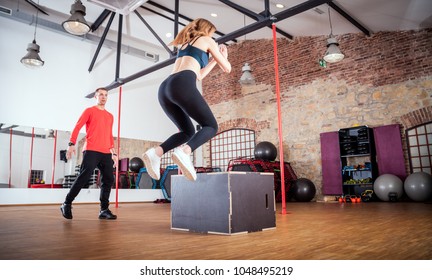 Fit Woman With Her Personal Trainer Doing Box Jump Exercise At Fitness Gym