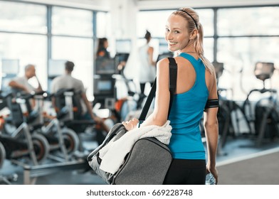 Fit Woman Holding Gym Bag In A Fitness Centre. Beautiful Blonde Woman Ready To Start Her Training. Portrait Of Energetic Woman Looking At Camera Ready For New Inscription At The Gym.