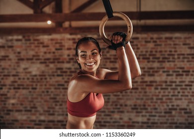 Fit woman holding gymnast rings at the gym and smiling. Young female exercising at gym with gymnastics rings. - Powered by Shutterstock