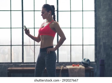 A fit woman is looking down at her device, seeing which song is going to give her the next rhythms for her workout.