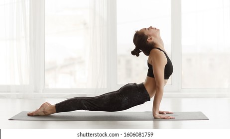 Fit woman making cobra pose on yoga mat, exercising in studio over panoramic window - Shutterstock ID 1606081759