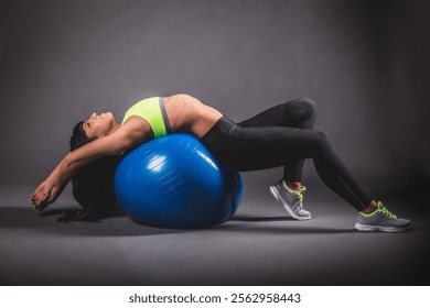 A fit woman in neon activewear stretching on a blue stability ball during a studio workout session, emphasizing core strength, flexibility, and relaxation. Perfect for fitness and wellness themes - Powered by Shutterstock