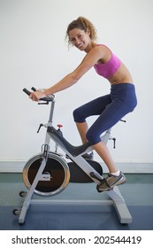 Fit Woman On The Spin Bike Smiling At Camera At The Gym