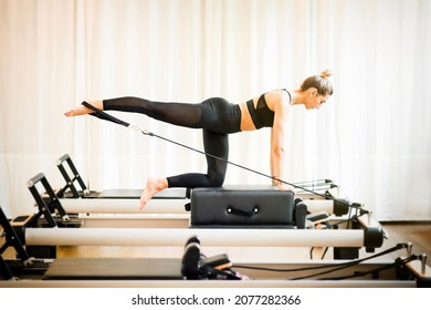 Fit woman performing a pilates diagonal stabilisation exercise using a strap on a reformer bed in a gym in a fitness concept - Powered by Shutterstock