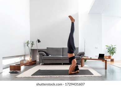 Fit woman practicing a headstand exercise, (salamba sirsasana pose) at her cozy home