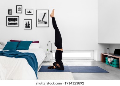 Fit woman practicing a headstand exercise, (salamba sirsasana pose) at her cozy home