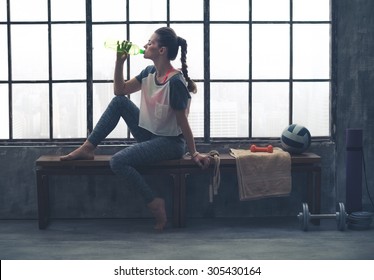 Fit woman in profile sitting on bench in loft gym drinking water. After a good workout, it's important to hydrate. - Shutterstock ID 305430164