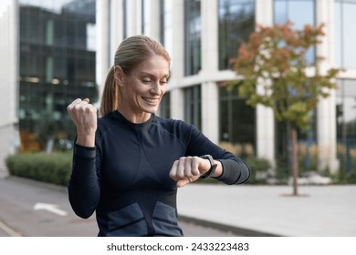 A fit woman with a smile checks her fitness tracker outdoor, exuding happiness and a healthy lifestyle. With a backdrop of urban architecture, this image captures the essence of active living in the - Powered by Shutterstock