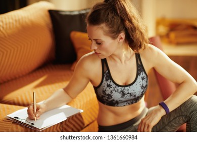 Fit Woman In Sport Clothes With Diary And Pen Building Workout Schedule In The Modern House.