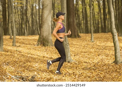 Fit woman in sports bra, black cap, and black leggings jogging through an autumn forest, surrounded by fallen leaves during an outdoor workout. - Powered by Shutterstock