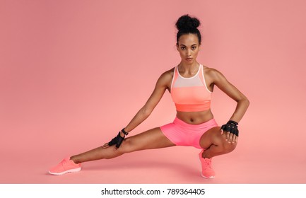 Fit woman stretching her leg to warm up on pink background. Sportswoman exercising in studio. - Powered by Shutterstock