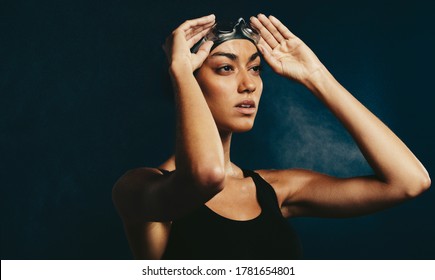 Fit woman in swimwear with swimming goggles looking away. Professional female swimmer on dark background. - Powered by Shutterstock