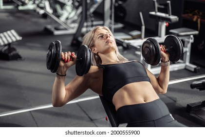 Fit woman trains chest muscles, doing bench press with dumbbells in hands while lying on an incline bench in the gym - Powered by Shutterstock