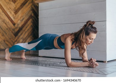 Fit woman working on abdominal muscles doing plank exercise, core workout at home.