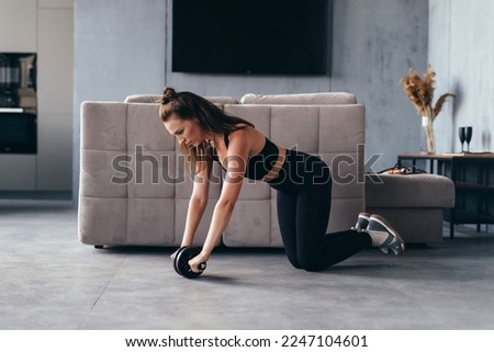 Fit woman working out with ab exercise wheel at home.