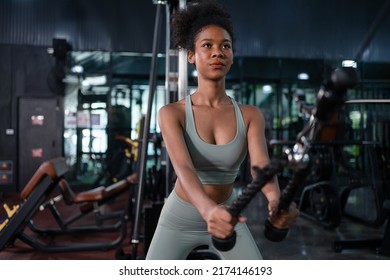 Fit young African American female athlete in sportswear exercise bodybuilder pulling down wire cable on gym equipment in fitness center.Workout for good health concept. - Shutterstock ID 2174146193