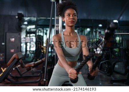Fit young African American female athlete in sportswear exercise bodybuilder pulling down wire cable on gym equipment in fitness center.Workout for good health concept.