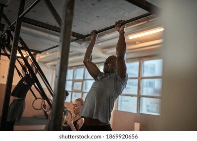 Fit Young African American Man In Sportswear Sweating While Doing Pull-ups During A Workout Session In A Gym