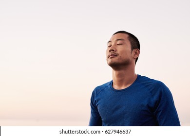 Fit Young Asian Man In Sportswear Standing With His Eyes Closed Outside While Taking A Break From An Early Morning Run