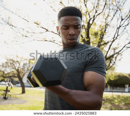 Fit young black man in t-shirt and wireless earphones doing bicep curl with dumbbell in park
