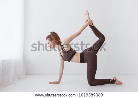 Fit young Caucasian woman practicing yoga at home standing in cat and cow pose arching her back. Raise your leg above your head. Lifestyle.