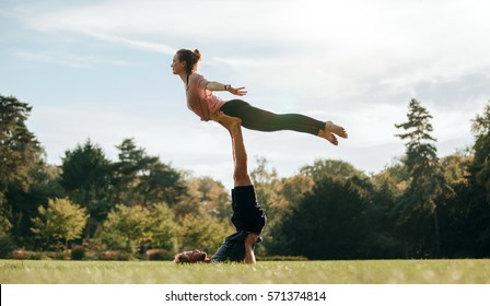 Fit young couple doing acro yoga in park. Man lying on grass and balancing woman in his feet. - Powered by Shutterstock