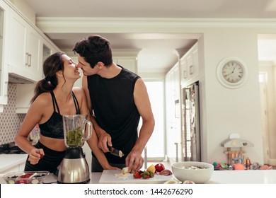 Fit young couple in love preparing healthy smoothie in kitchen. Couple about to kiss while preparing healthy breakfast in kitchen. - Powered by Shutterstock