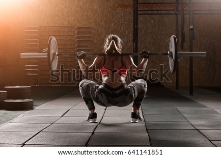 Fit young girl with light brown hair wearing black leggins, pink top and sneakers and doing squats with barbell, dark gym at background, cross training workout, portrait. Foto stock © 
