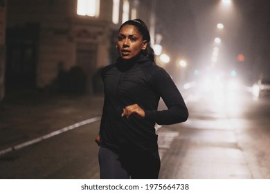 Fit young Indian woman in sportswear running along a road in the city at night illuminated by car lights - Powered by Shutterstock