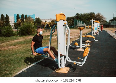 Fit Young Male Caucasian Athlete With Face Mask  Trains On Arm And Leg Equipment In An Outdoor Gym. Muscular Athlete Outdoors.  COVID - 19 Coronavirus Protection