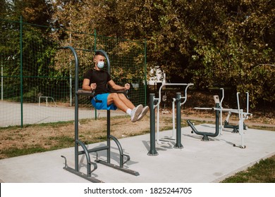 Fit Young Male Caucasian Athlete With Face Mask  Trains On Arm And Leg Equipment In An Outdoor Gym. Muscular Athlete Outdoors.  COVID - 19 Coronavirus Protection