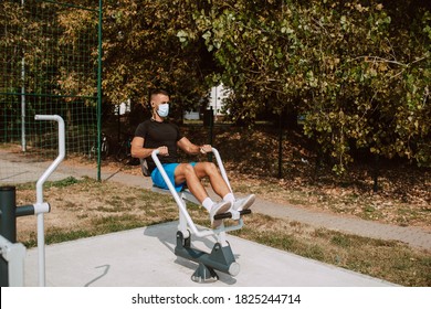 Fit Young Male Caucasian Athlete With Face Mask  Trains On Arm And Leg Equipment In An Outdoor Gym. Muscular Athlete Outdoors.  COVID - 19 Coronavirus Protection