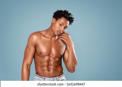 Fit young man with beautiful torso, isolated on blue pastel background. Naked torso of African American man posing at studio. Muscular body, fitness, sports, healthy lifestyle and bodybuilder concept.