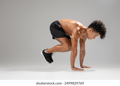 A fit young man engages in an athletic movement, focusing on strength and agility. He demonstrates a powerful stance in preparation for a dynamic workout, showcasing his dedication to fitness - Powered by Shutterstock