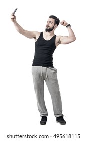 Fit Young Man Flexing Bicep Arm Muscle While Taking Selfie Photo With Mobile Phone. Full Body Length Portrait Isolated Over White Studio Background