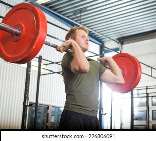 Fit young man lifting barbell at gym
