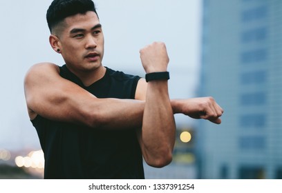 Fit Young Man With Muscular Build Standing Outside Stretching Hands And Looking Away. Asian Fitness Model Doing Warmup Workout.