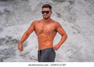 Fit young man posing confidently on a sunny beach in summer. A muscular man stands on a beach, showcasing his physique while enjoying the sunny weather. - Powered by Shutterstock