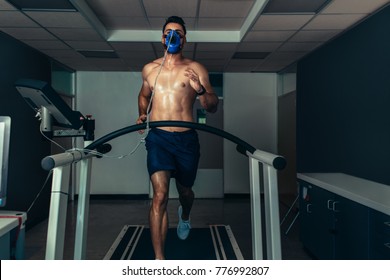 Fit Young Man Running On Treadmill With A Mask In Sports Lab. Athlete Examining His Performance In Sports Science Lab.