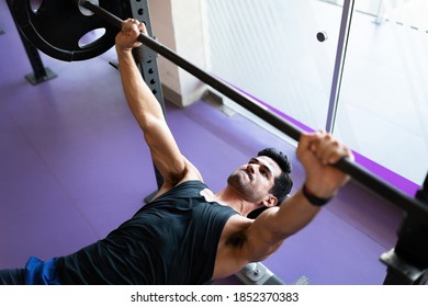 Fit Young Man Seen From Above Fixed On Lifting A Heavy Barbell And Lying On A Gym Bench