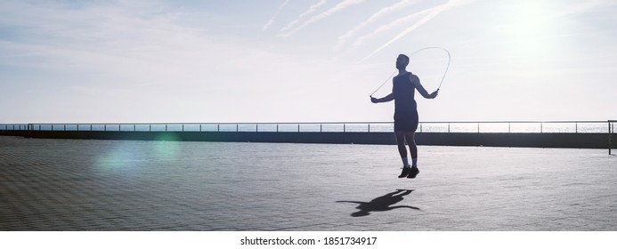 Fit Young Man Skipping With A Jump Rope Outdoors. Male Athlete Doing Fitness Training In Morning. Workout During Lockdown Outside The Gym.