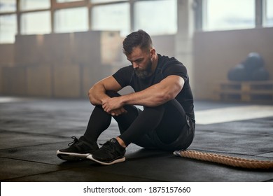 Fit Young Man In Sportswear Sitting On A Gym Floor And Looking Exhausted After A Battle Rope Workout Session