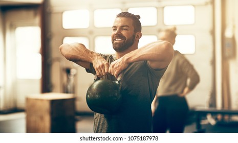 Fit Young Man In Sportswear Smiling And Lifting Dumbells During An Exercise Class In A Gym