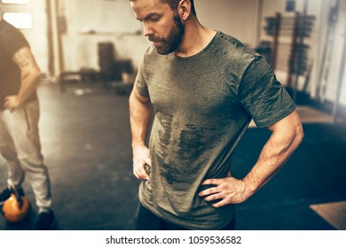 Fit young man in sportswear standing with his hands on his hips in a gym sweating after a workout session